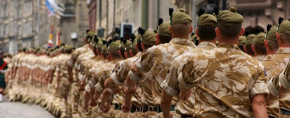 Soldiers in desert camouflage uniform marching in formation along a street